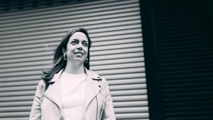 A person standing in front of a shop shutter smiling as they look off camera