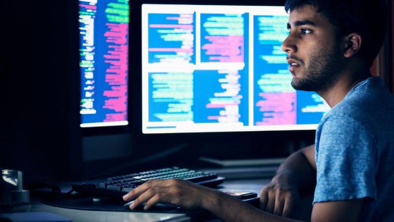 young male sitting in front of two computer monitors