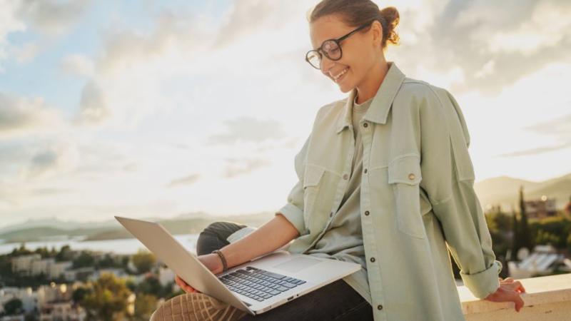 female sitting outside looking at a laptop screen and smiling