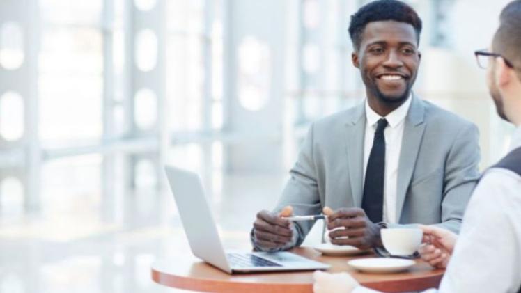 two men sitting chatting in suits at a desk