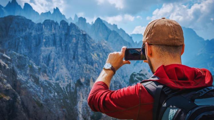 male student standing taking a photo of a mountain