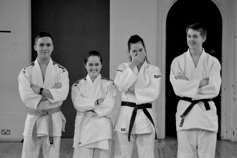 Black and white shot of four judo players, one player has begun to laugh