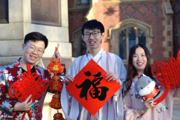 Three students hold up symbols of good luck for the Chinese New Year in traditional dress