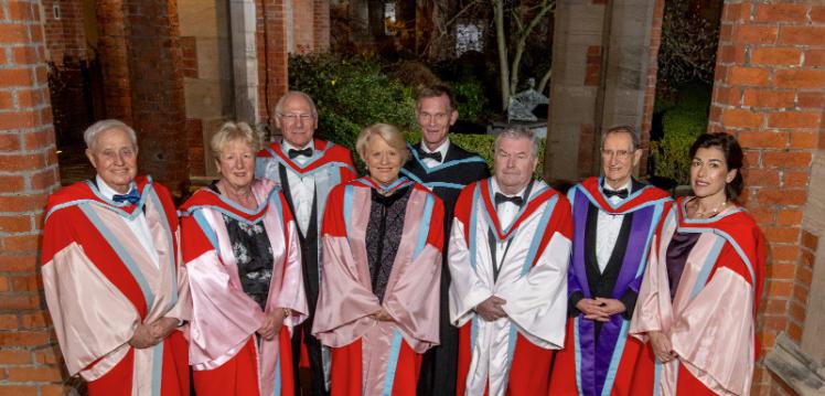 Eight honorary grads dressed in graduation robes in the Cloisters