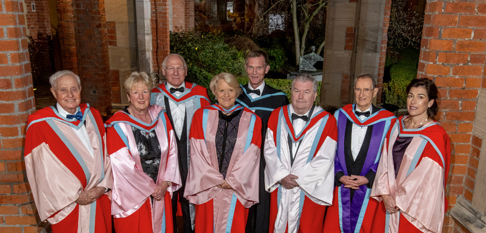 Eight honorary grads dressed in graduation robes in the Cloisters