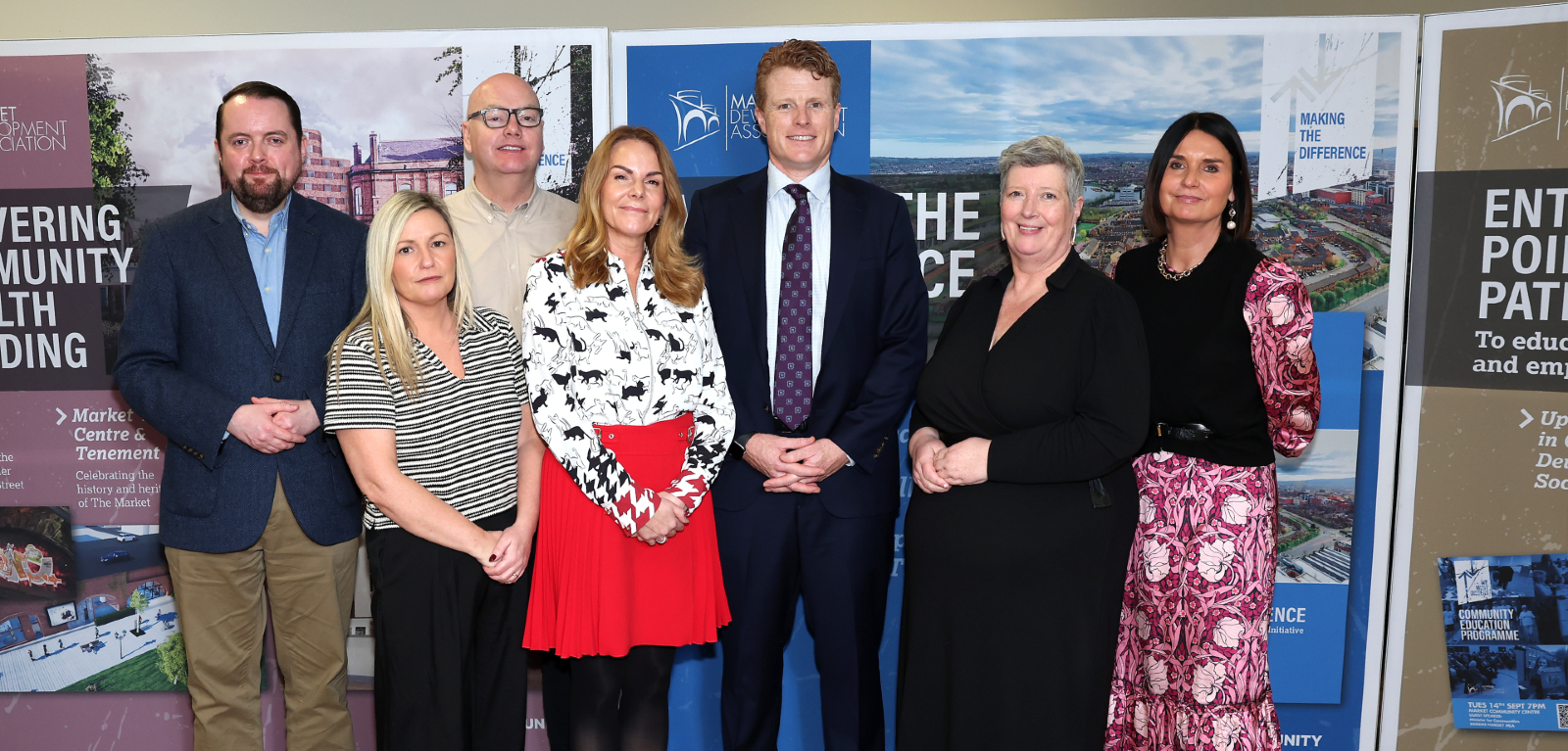 A group of people stand posed in front of banners in a community hall looking towards the camera.