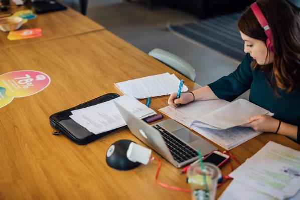 Student writing notes at desk with headphones on