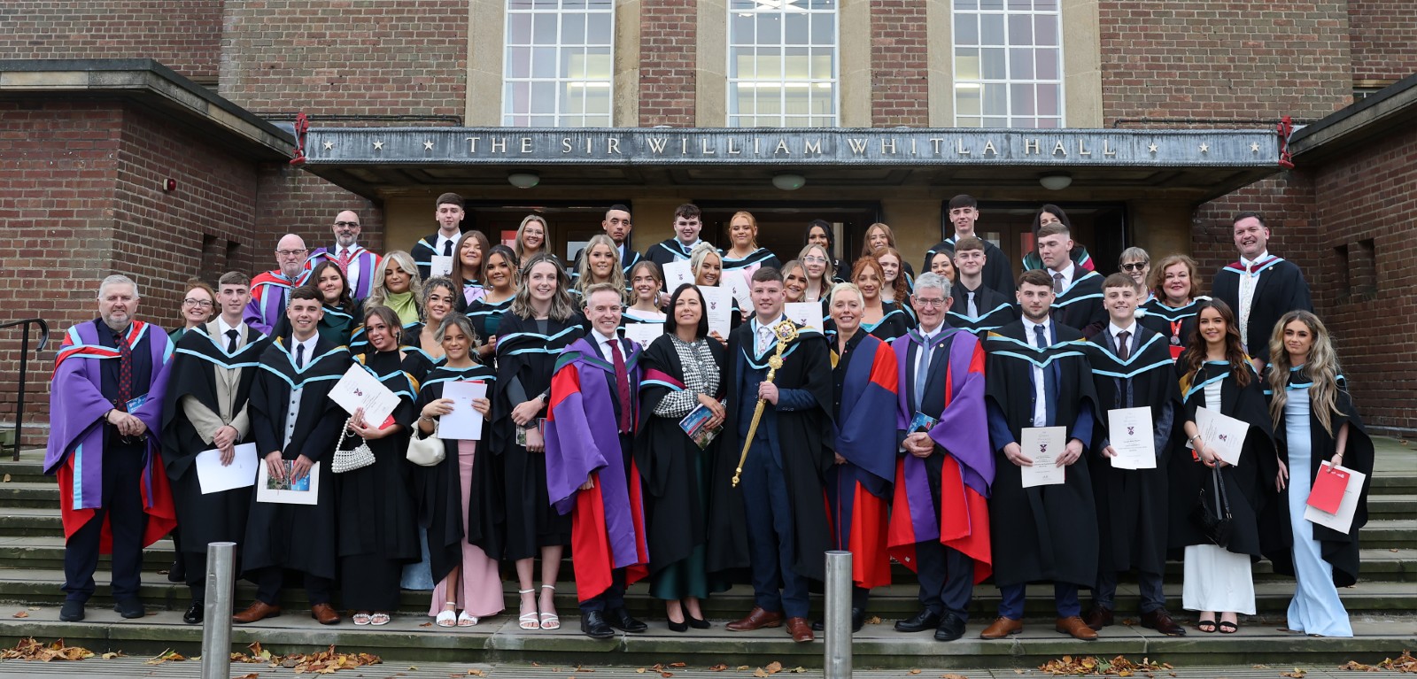 A group of graduates and academics gathered on steps looking at the camera