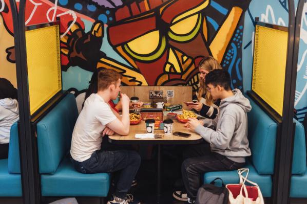 Four students sit in booth in Reboot cafe eating chips