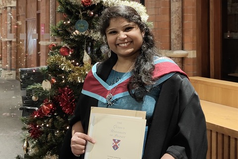 Student Sai Sree with her certificate, standing in front of a Christmas tree in the Graduate School