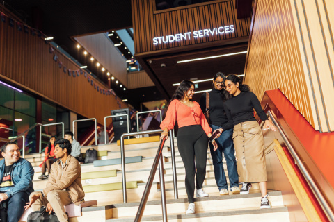 Three female students walking down stairs in One Elmwood in front of Student Services sign
