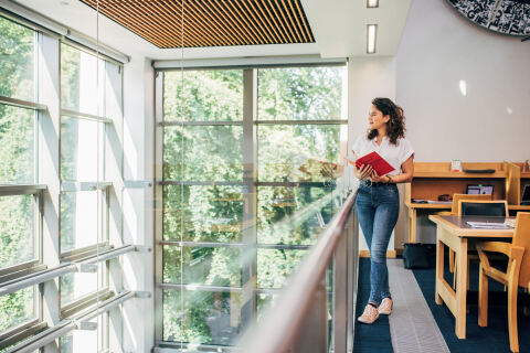 Student standing in the McClay Library holding a red book