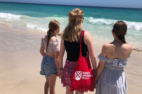 Female student with Queen's tote bag standing beside two other females on beach