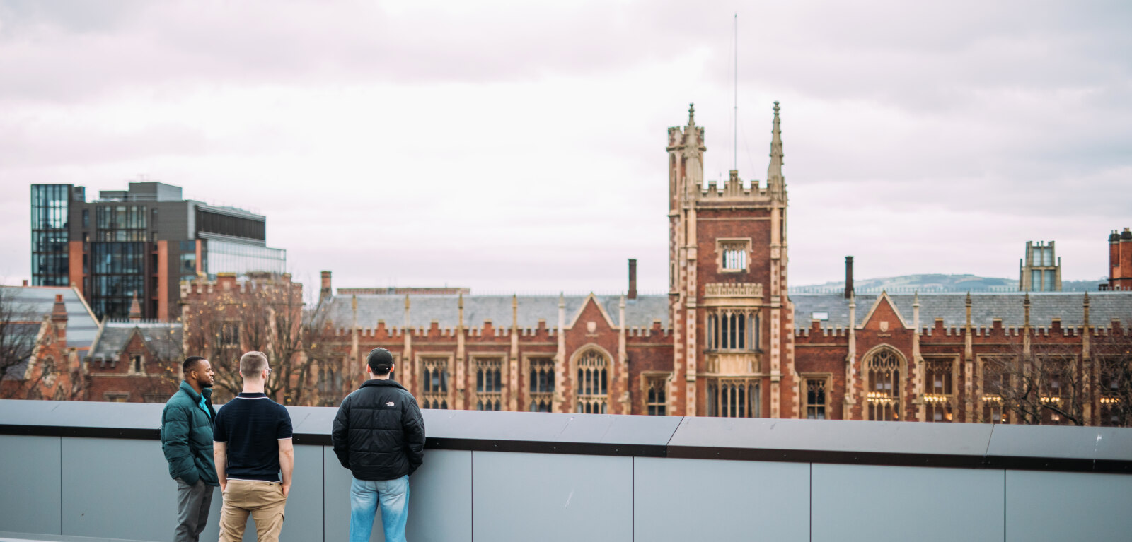 Three QUB students look at the Lanyon building from the roof of One Elmwood