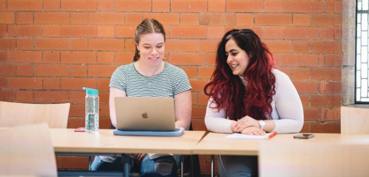 Two female students work together in front of laptop