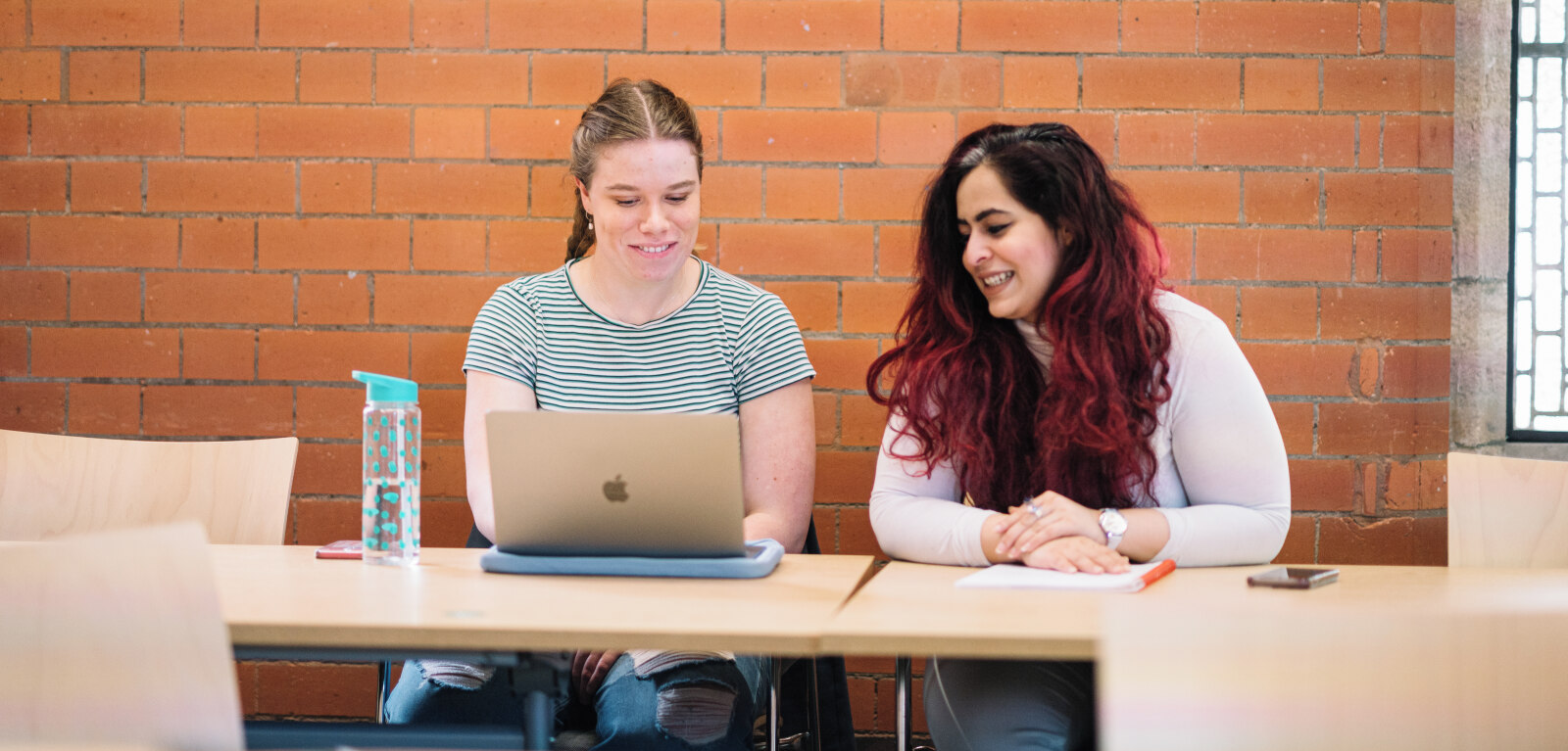 Two female students work together in front of laptop