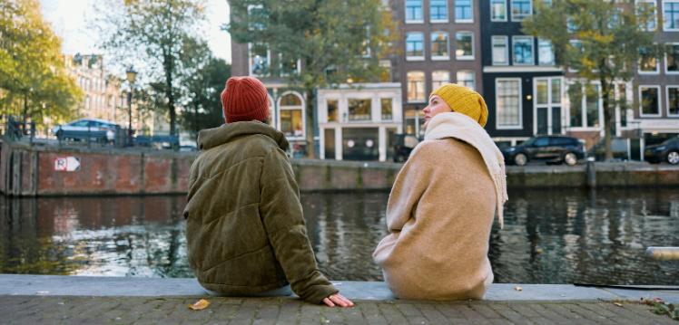 Two people in coats and hats sitting by a river