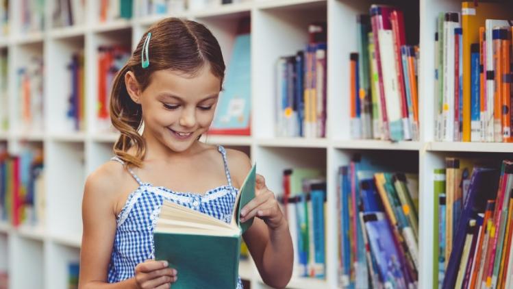 young girl in sundress reading a book in library