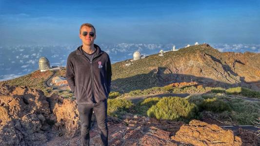 Student standing on a mountain observatory surrounded by telescopes