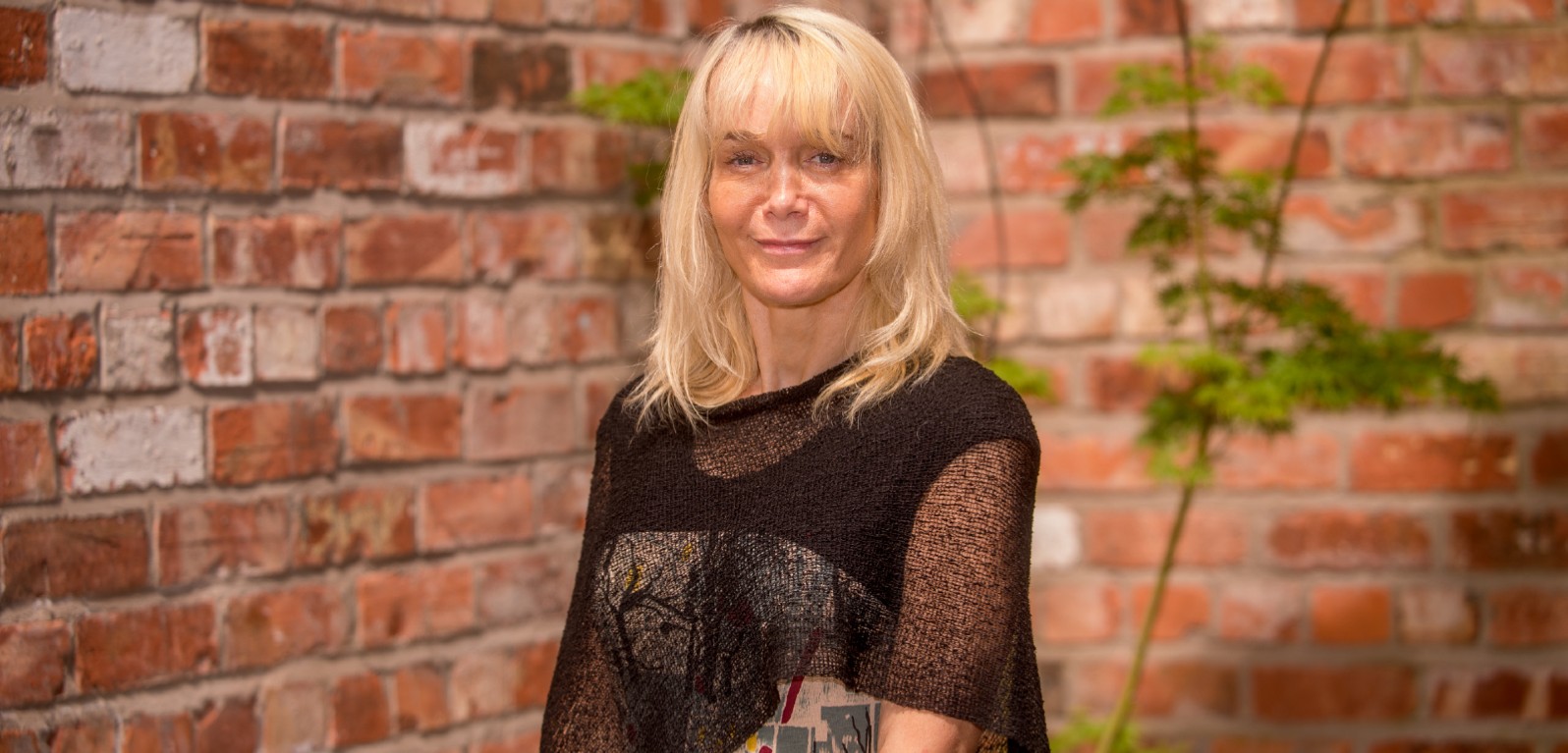 blonde woman in black top against a red brick wall