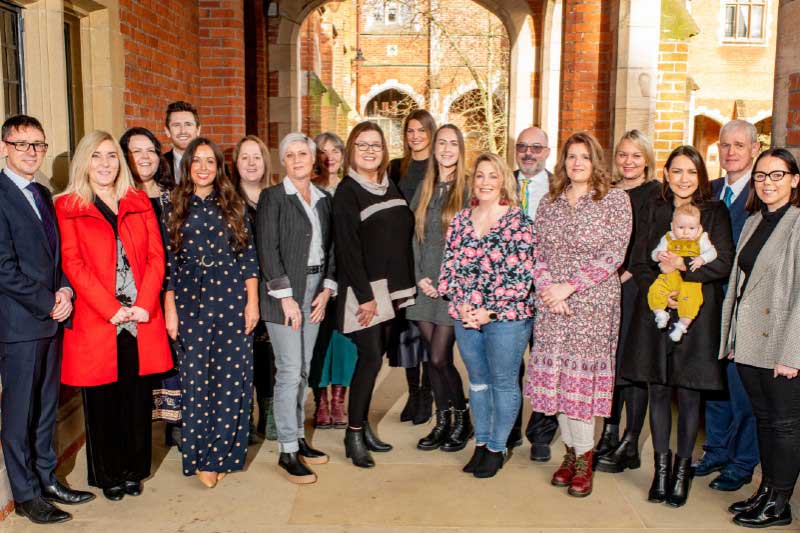 18 men and women in a row against a red brick background