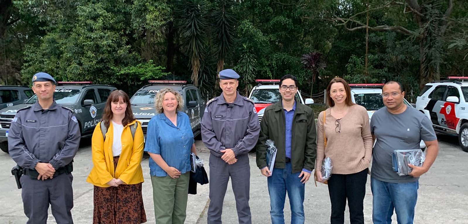 two uniformed male police officers, three female academics and two male academics, standing ina row in front of police cars