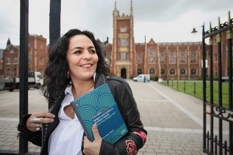 smiling woman with shoulder length dark wavy hair, holding a book