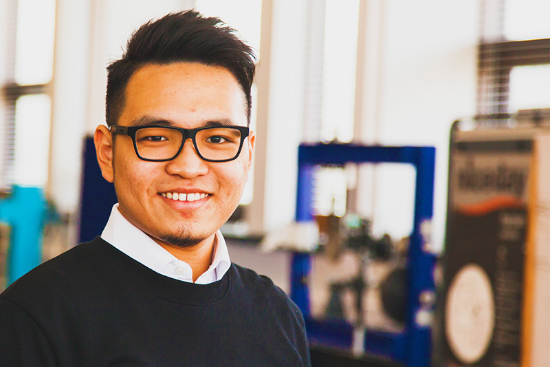 close up of a smiling male student wearing glasses with mechanical equipment in the background