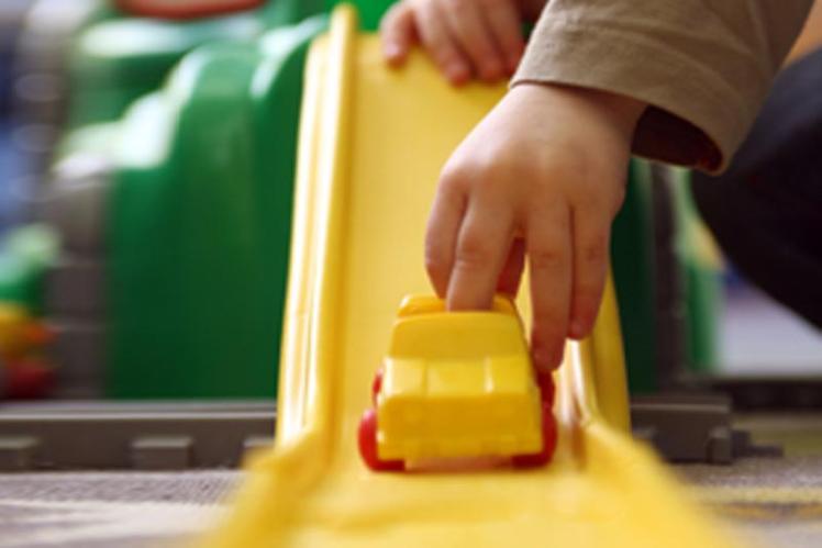 Child's hand playing with a yellow toy car