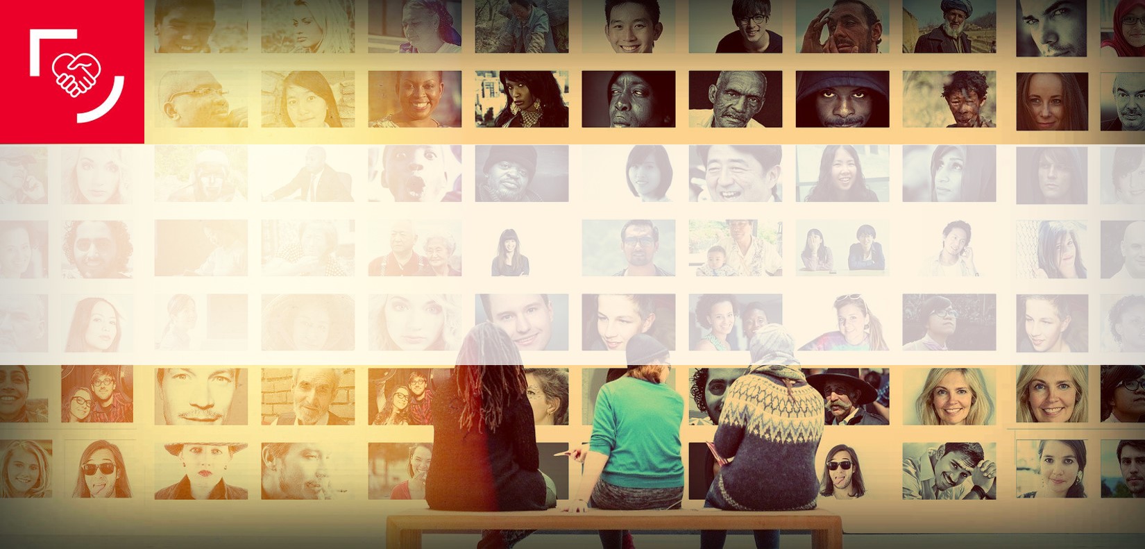 Three students on a bench watch a wall comprising dozens of face pictures of people from all nationalities