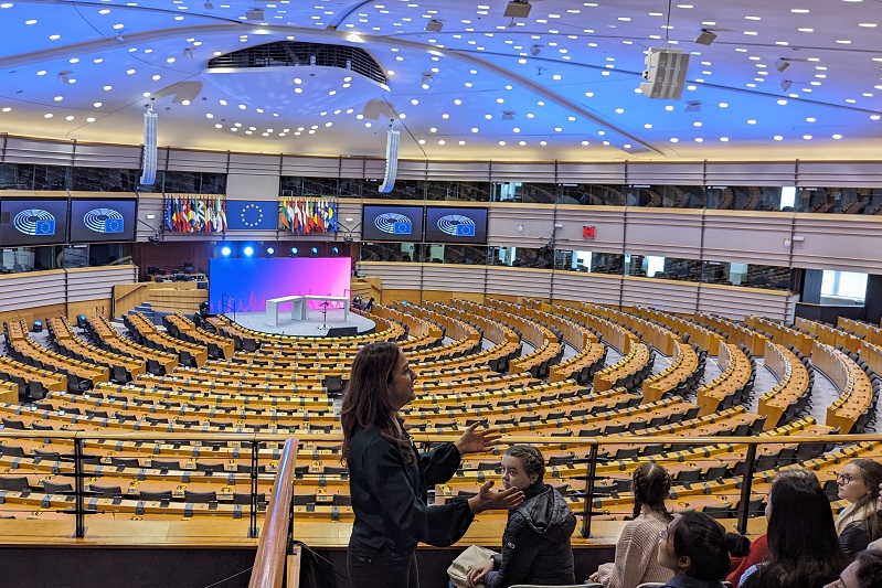 empty parliament chember with a person giving a talk to some students in the foreground