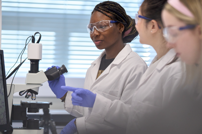 a group of Biomedical Sciences students wearing white lab coats standing beside lab equipment