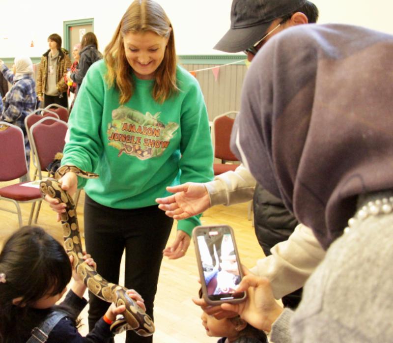 Child holding a snake whilst adults look on and one takes a photo on their phone.