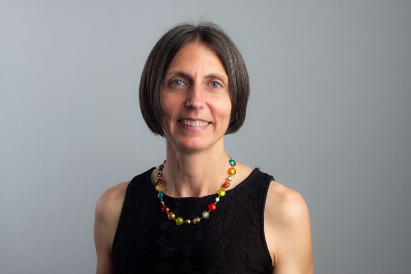 a smiling dark-haired woman wearing a black top and coloured necklace