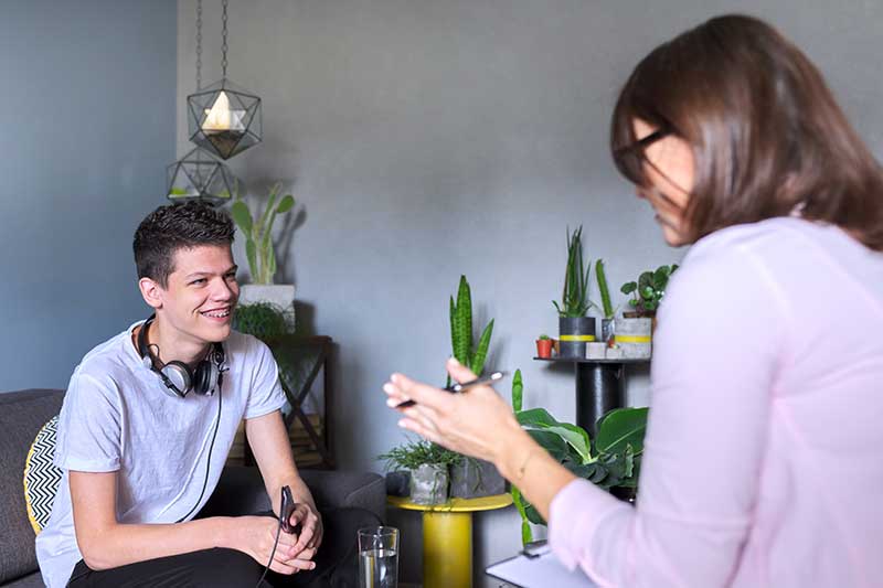 a seated young man smiling up at a woman with a clip board