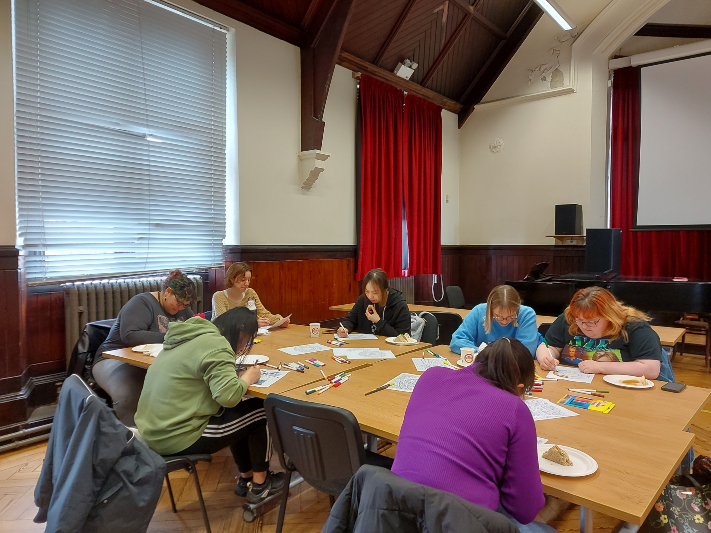 Group of people sitting at a table colouring pictures with some eating.