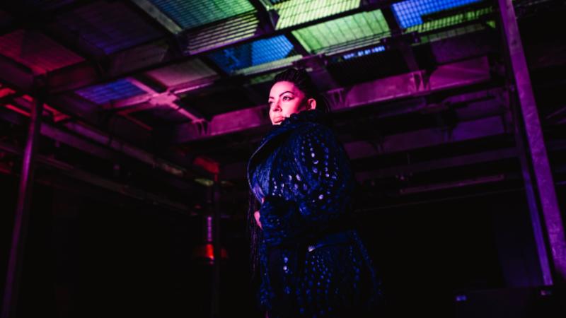 person standing looking off camera inside a dark studio with lights in the background