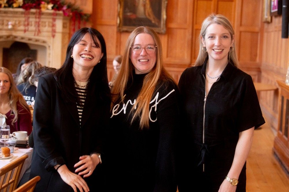 three young women smiling to camera at an indoor event in a bright, old, wood-paneled space