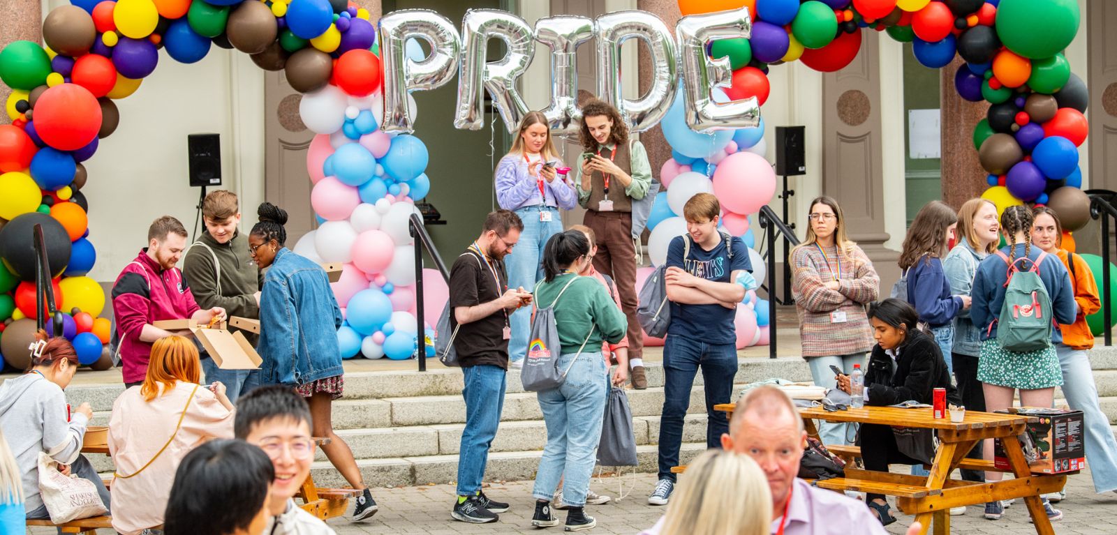 Staff and students in front of the Elmwood hall with Pride balloon backdrop