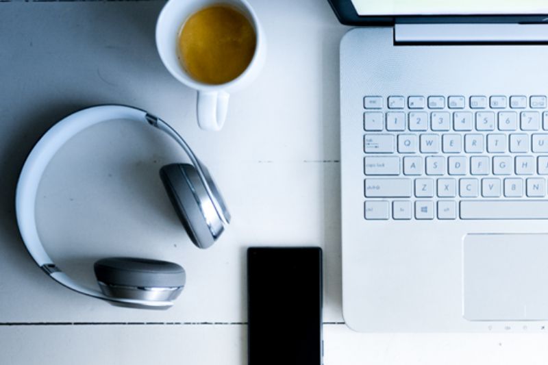 Image from above of laptop with headphones, coffee and iPhone on a white desk.