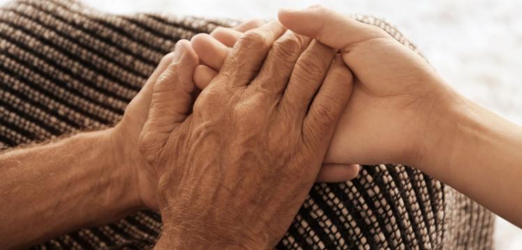 A photograph of two hands holding against brown fabric in a caring way.