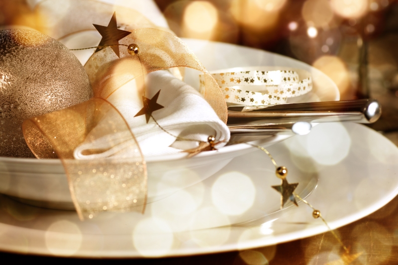 Christmas decorative items sitting on top of white crockery and cutlery in a cosy dinner setting