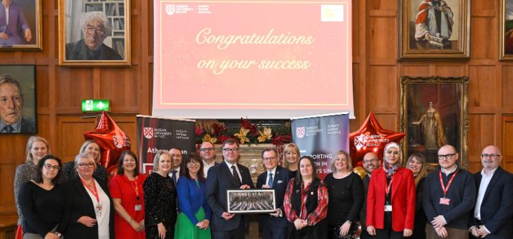 large group of people posing for an award photograph in an old hall with paintings hanging on the wood-paneled walls and a projector screen reading 'Congratulations on your success'