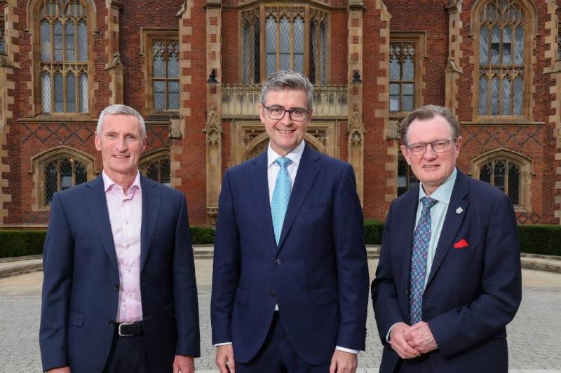three men in navy-blue business dress smiling to camera in front of an old redbrick building