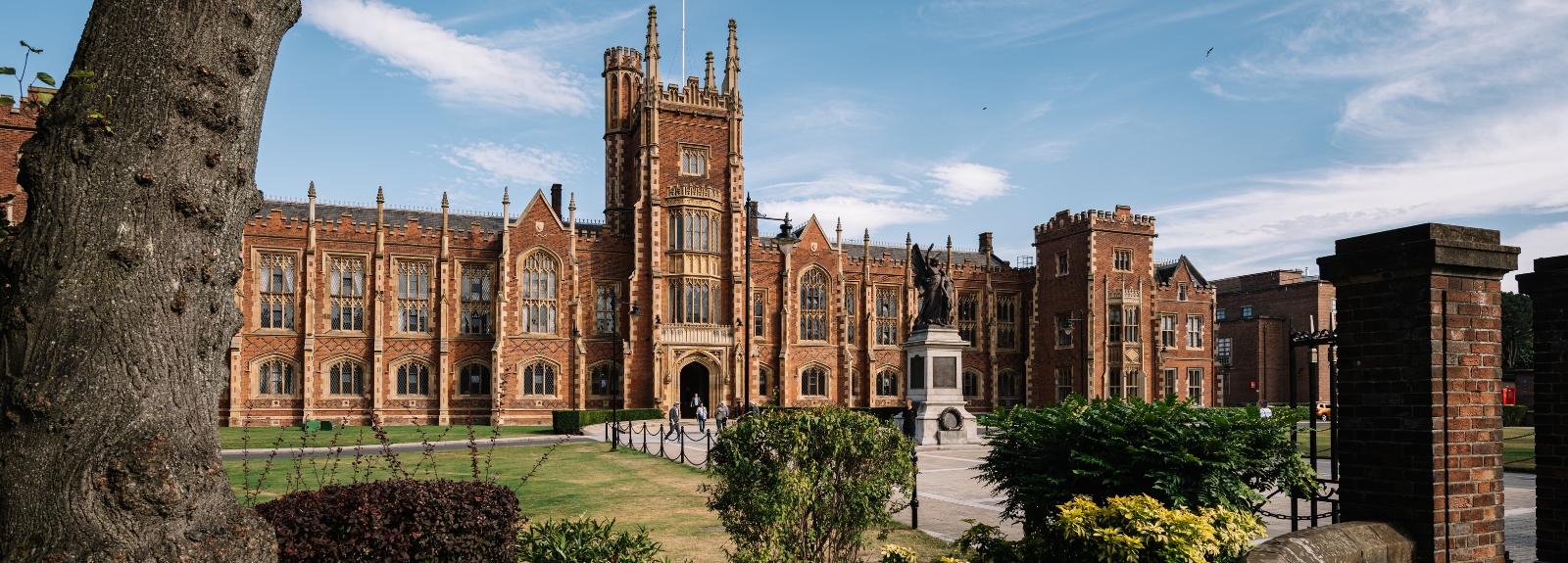 Queen's University Belfast Lanyon Building viewed from outside the front gate, with tree trunk to the left and stone gatepost to the right