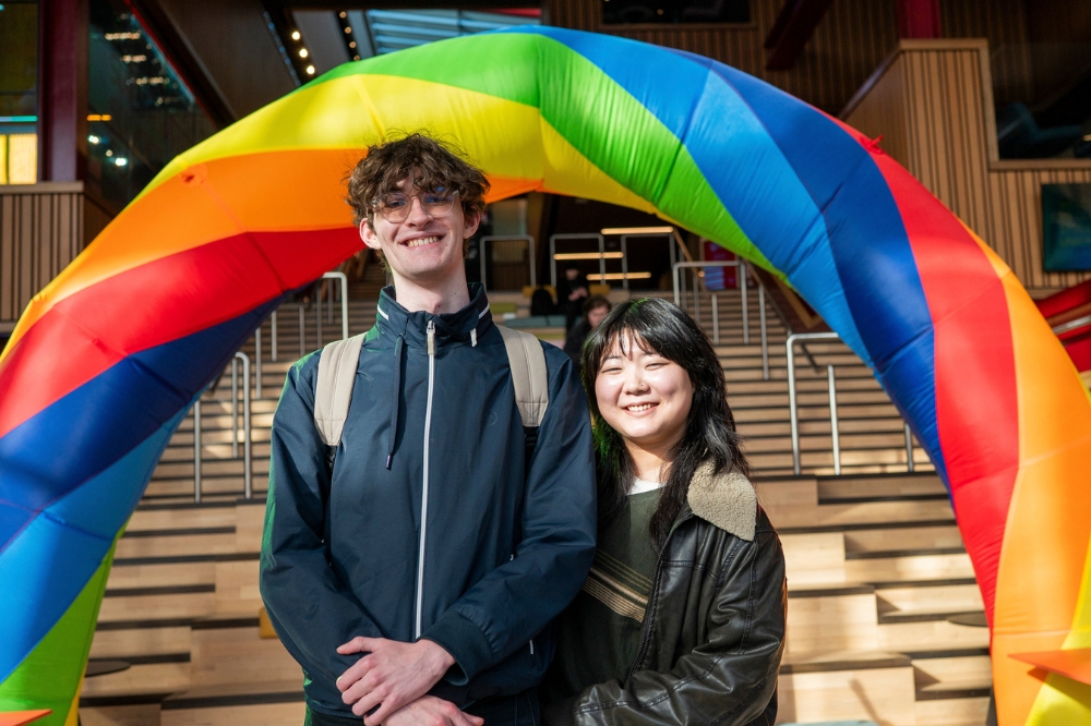 two students smiling under a rainbow arch at the LGBTQueen's Celebration Showcase event, One Elmwood