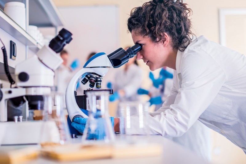 woman looking through a microscope in a lab