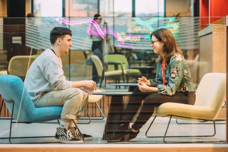 student and staff member chatting at a coffee table in an open space