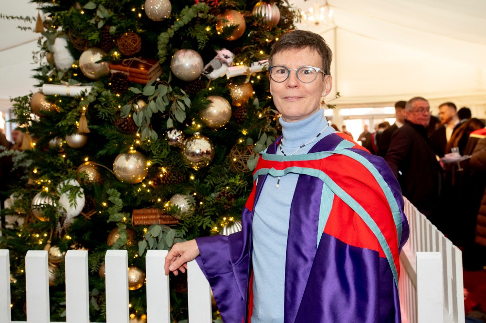 woman in graduation robe standing in front of a Christmas tree at a winter graduation